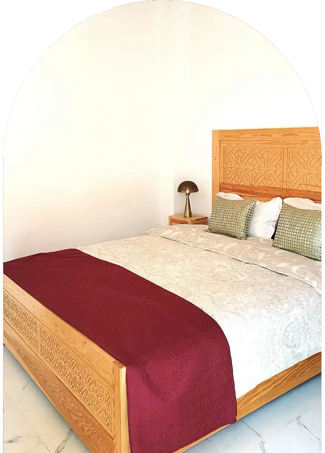 Lit marocain en bois sculpté avec linge soigné dans une chambre de riad à Essaouira